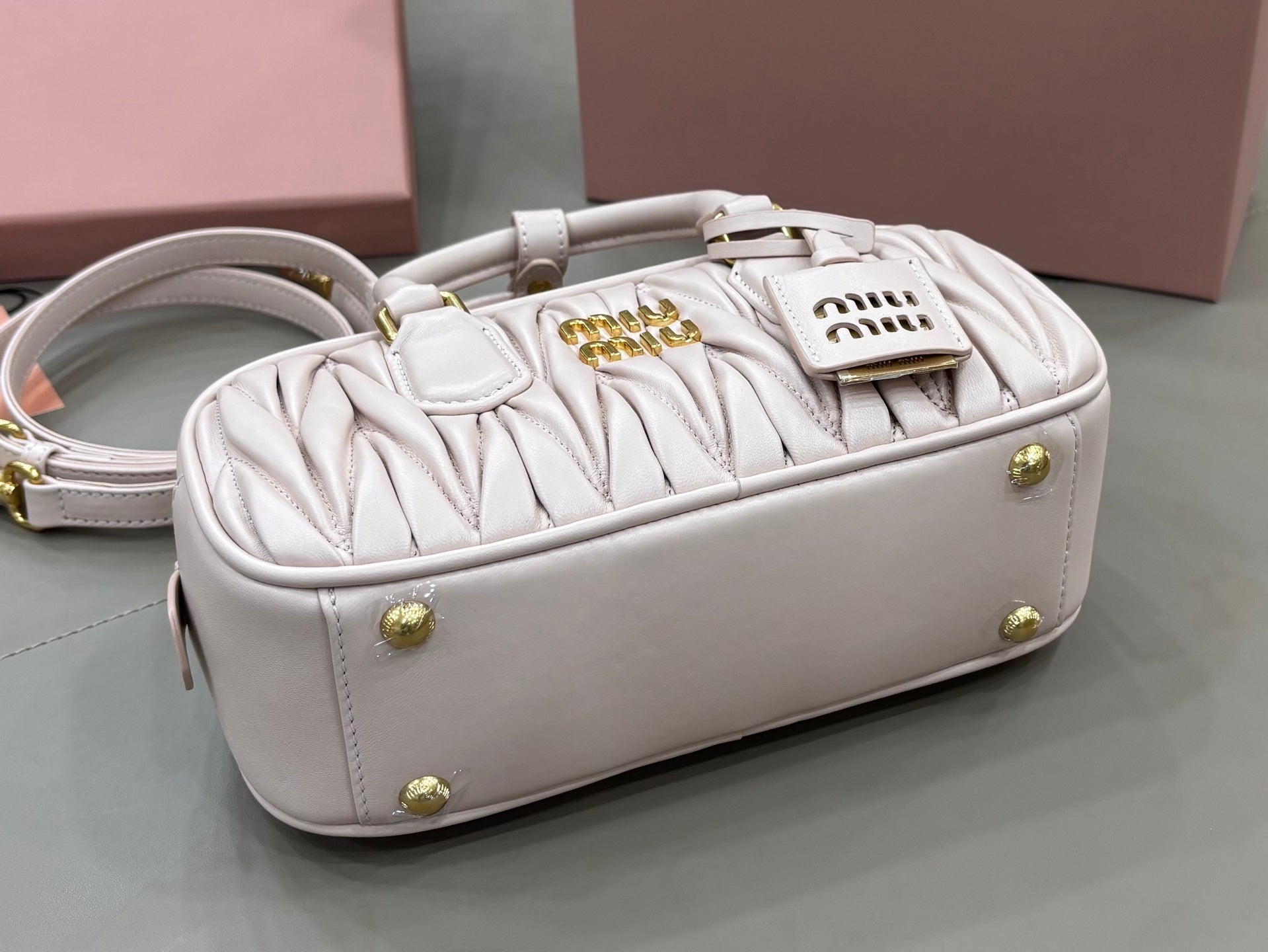 MiuMiu light gray mini bag with top handles, gold studs, and side view