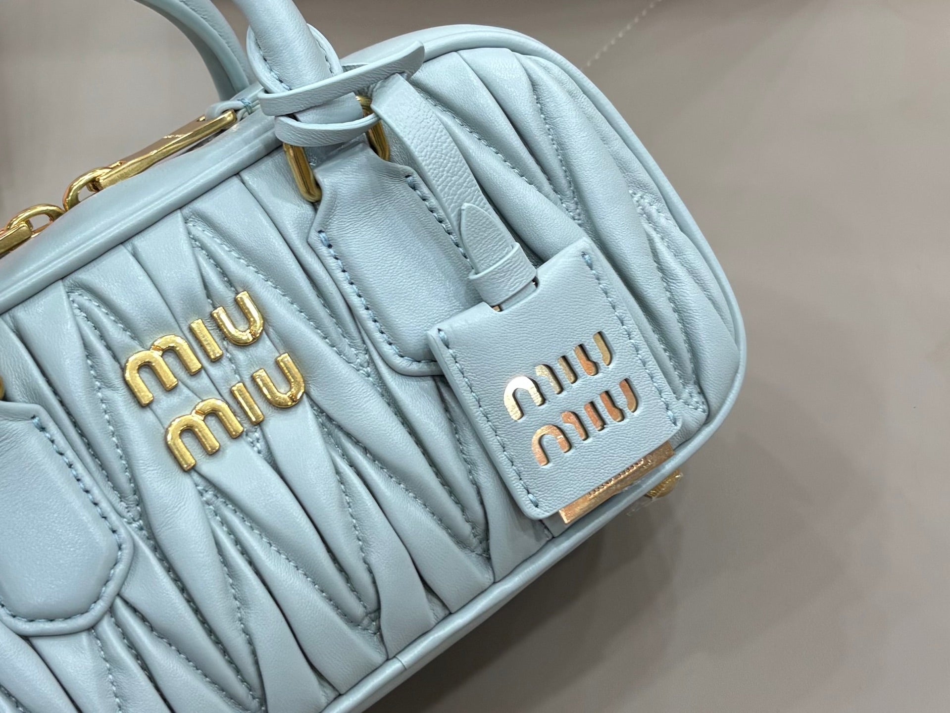 MiuMiu light blue quilted mini bag close-up of logo patch and stitched texture