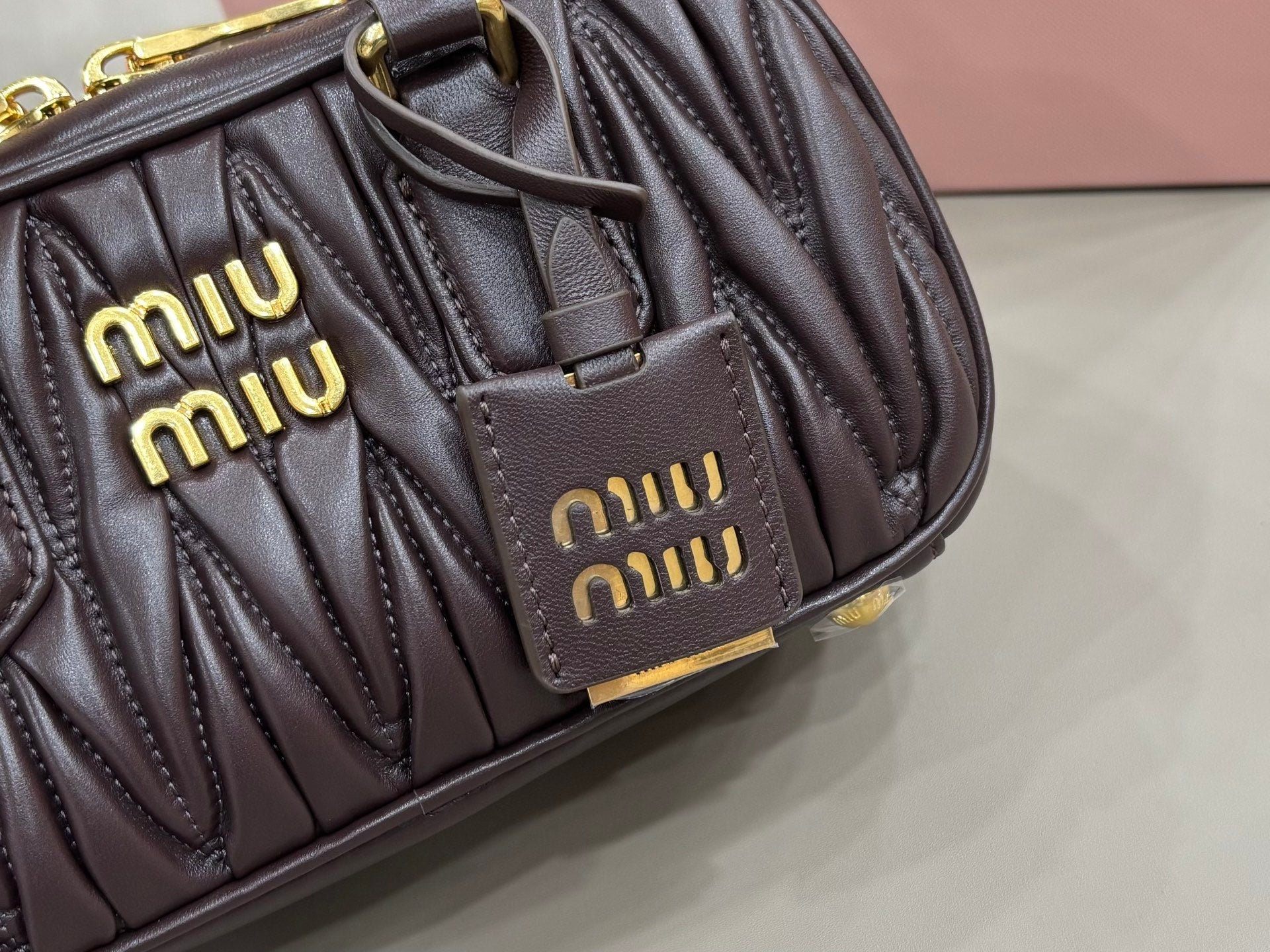 Dark brown quilted bag front close-up with two logo patches and gold hardware