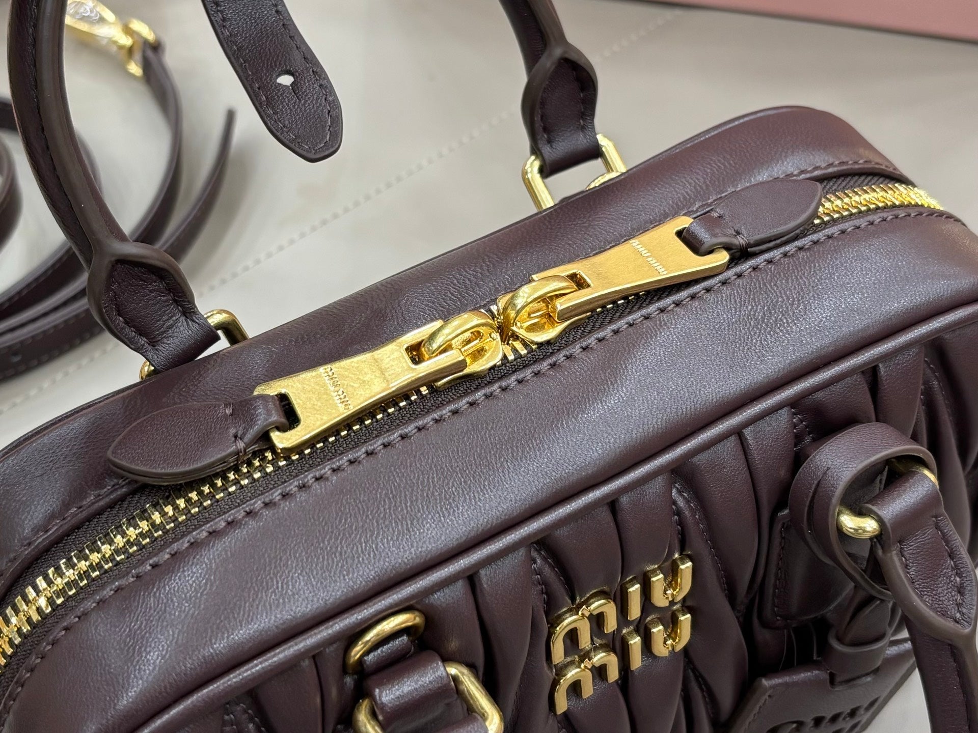 Dark brown mini top-handle bag close-up with gold zipper pull and logo