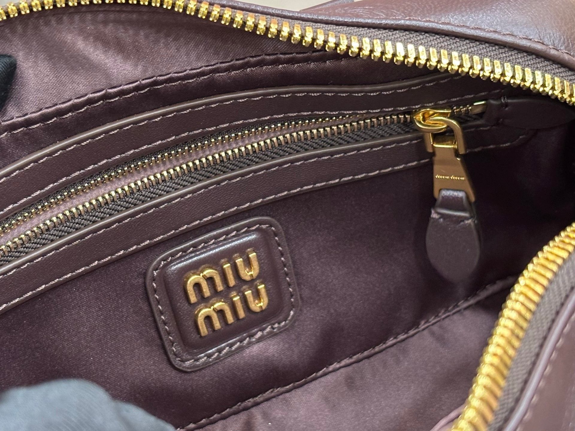 Dark brown bag interior close-up with gold zipper and small logo patch