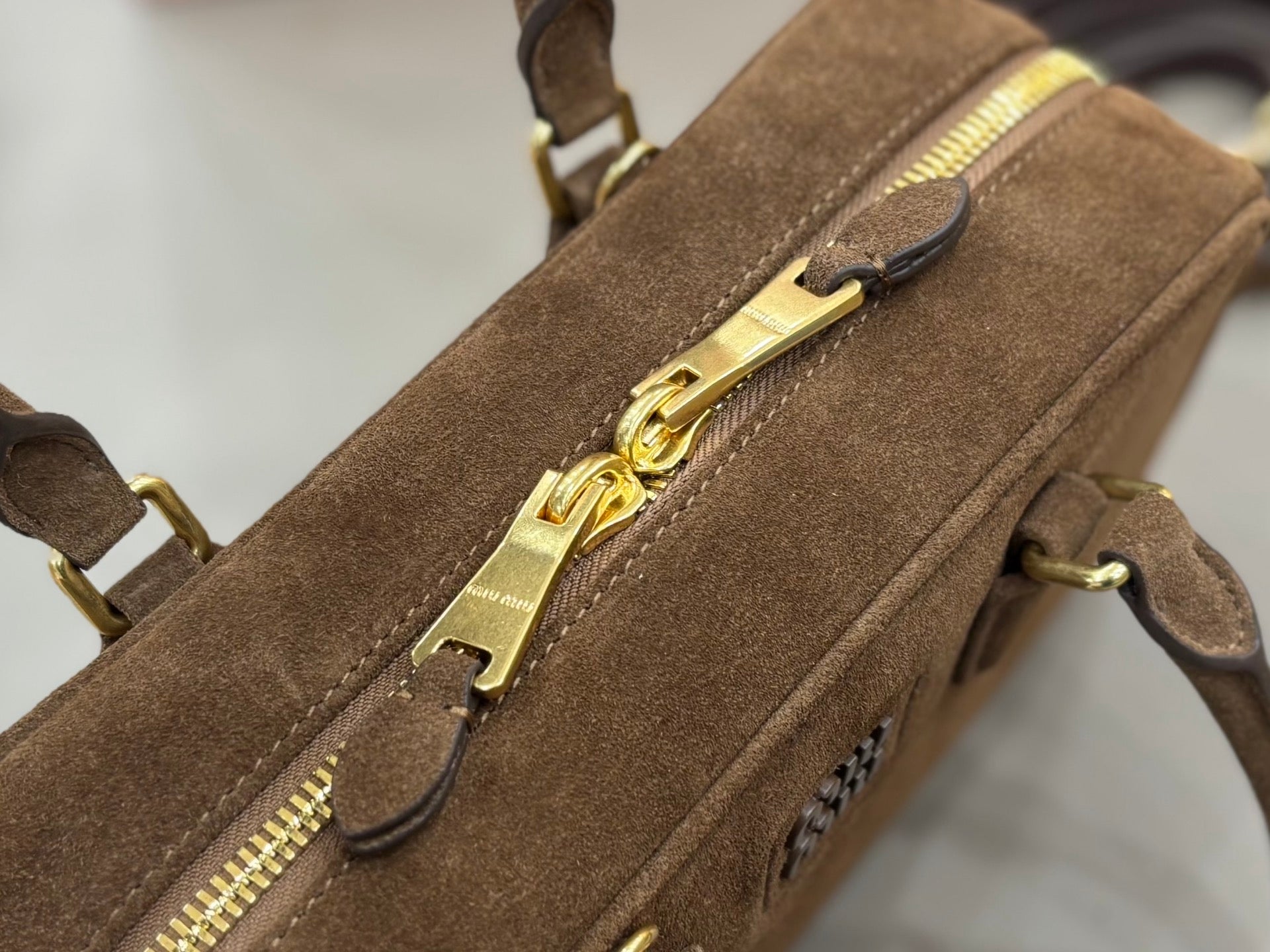 Front zipper detail on suede mini bag with gold-tone pull and side logo emblem