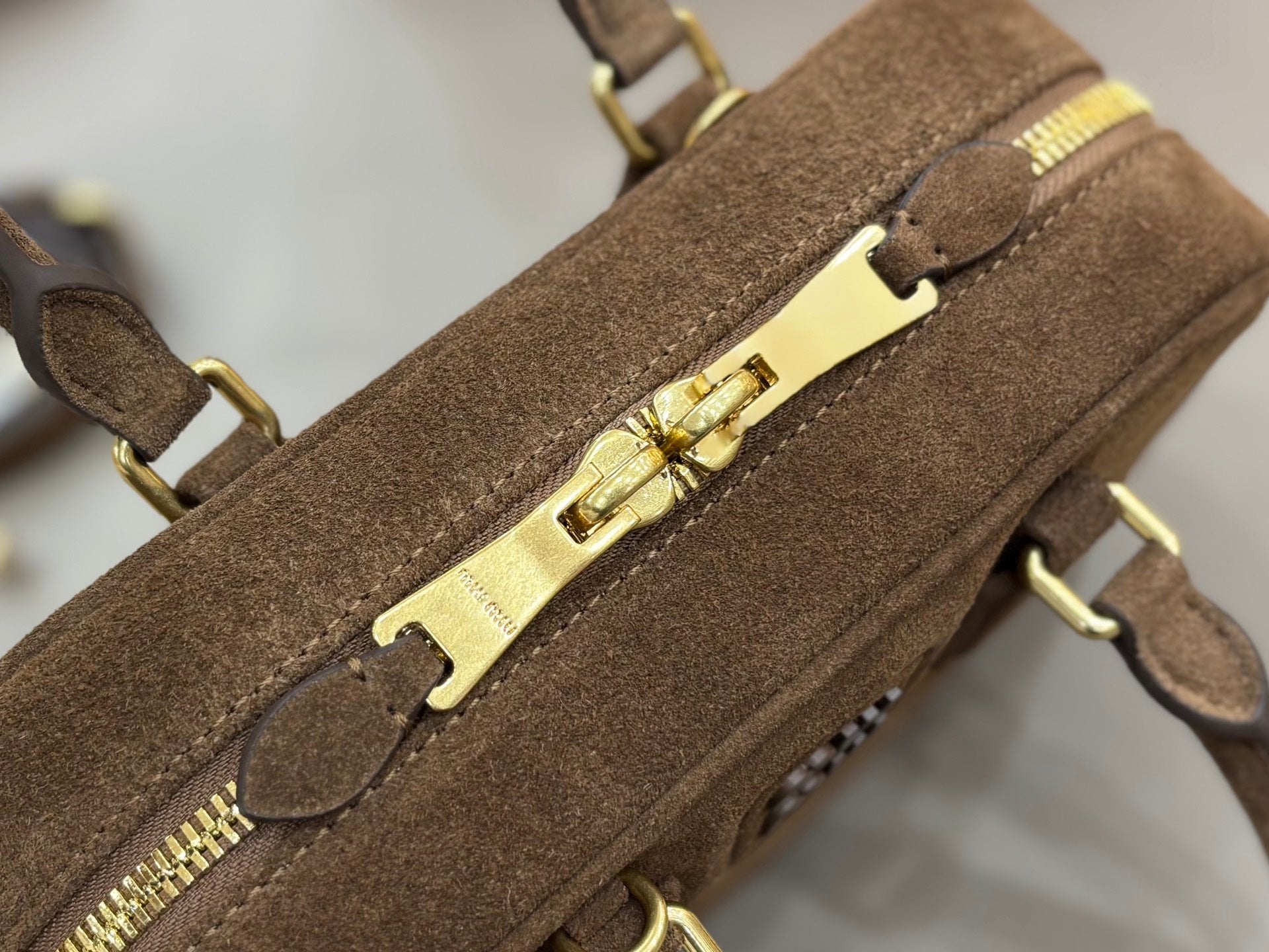 Suede mini handbag close-up of gold zipper hardware and front latch detail