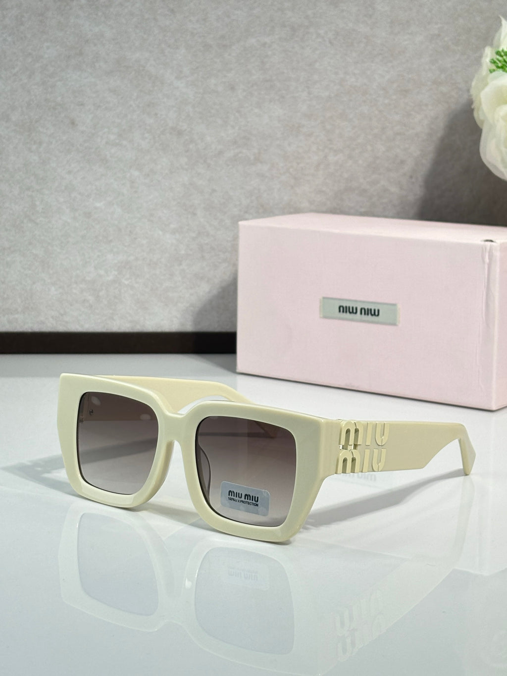 Square cream sunglasses with dark lenses and gold “miu miu” logo on the temple
