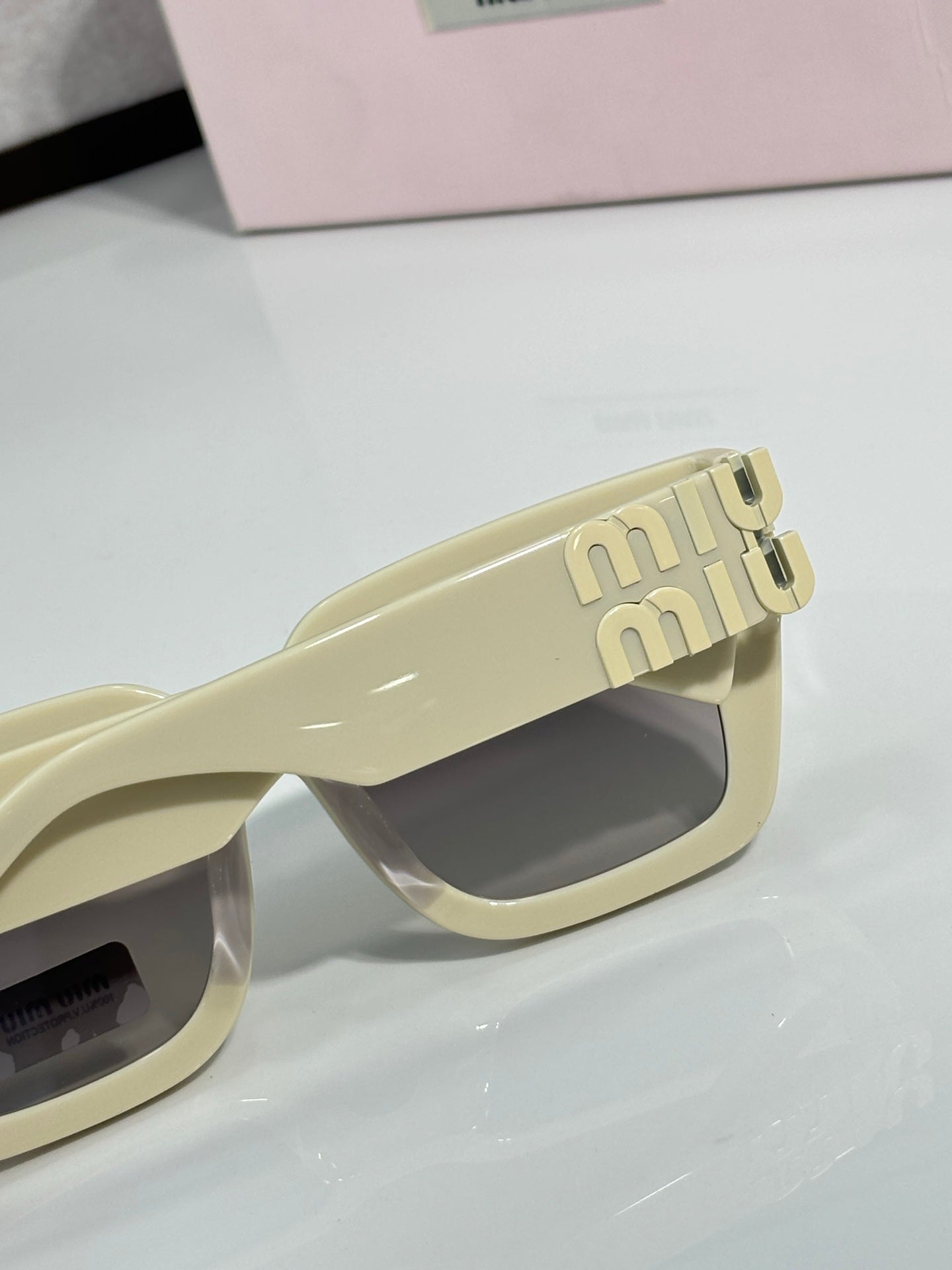 Cream square sunglasses with dark lens and embossed “miu miu” logo on the temple