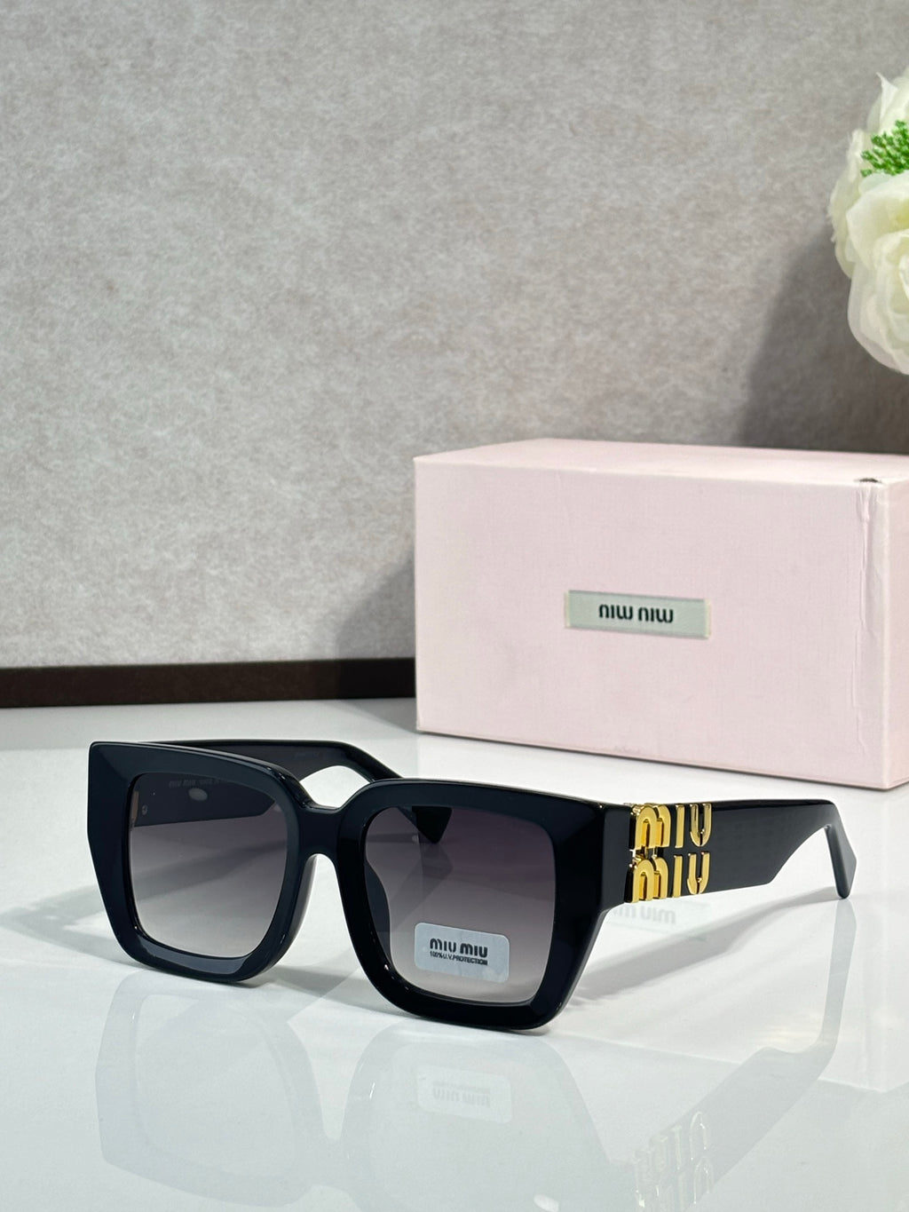 Square sunglasses with dark navy frames, black lenses, and gold logo at the temple