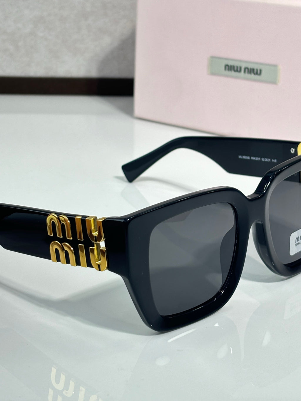 Dark navy square sunglasses with black lenses and gold “miu miu” logo on the temple