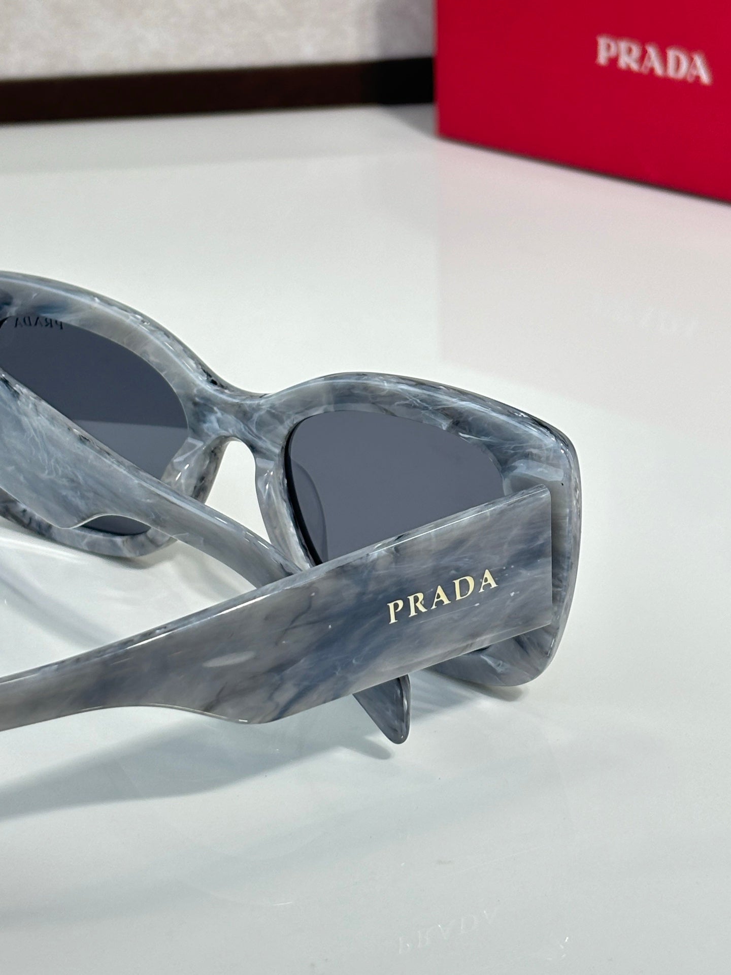 Prada gray marbled sunglasses with dark lenses and curved, angular frame