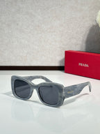 Prada gray sunglasses with dark lenses and translucent, curved frame
