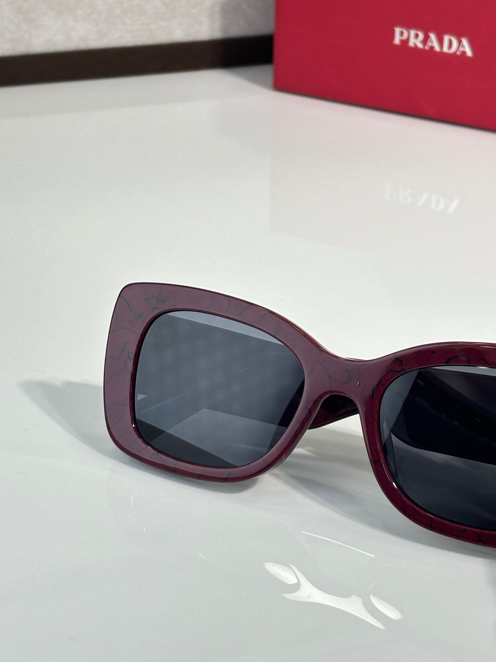 Prada maroon sunglasses close-up with dark lenses and curved frame