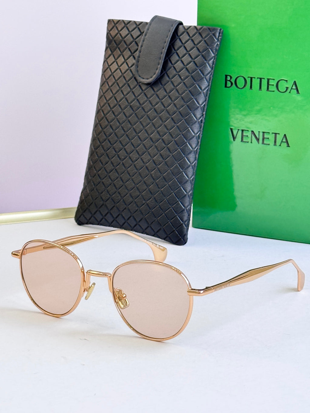 Round sunglasses with gold frame and light pink lenses, with black leather case