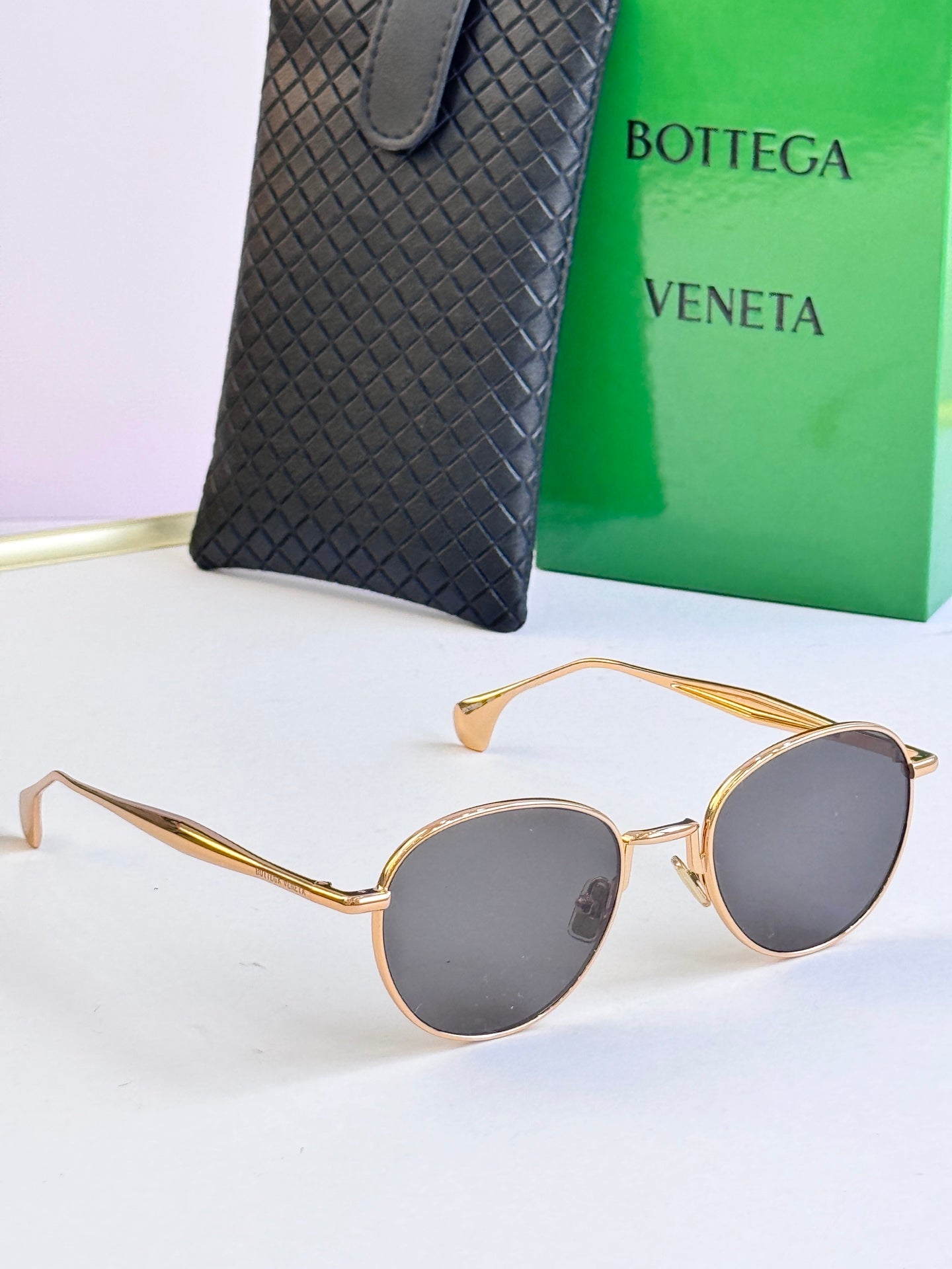 Round sunglasses with gold frame and dark gray lenses, with black leather case