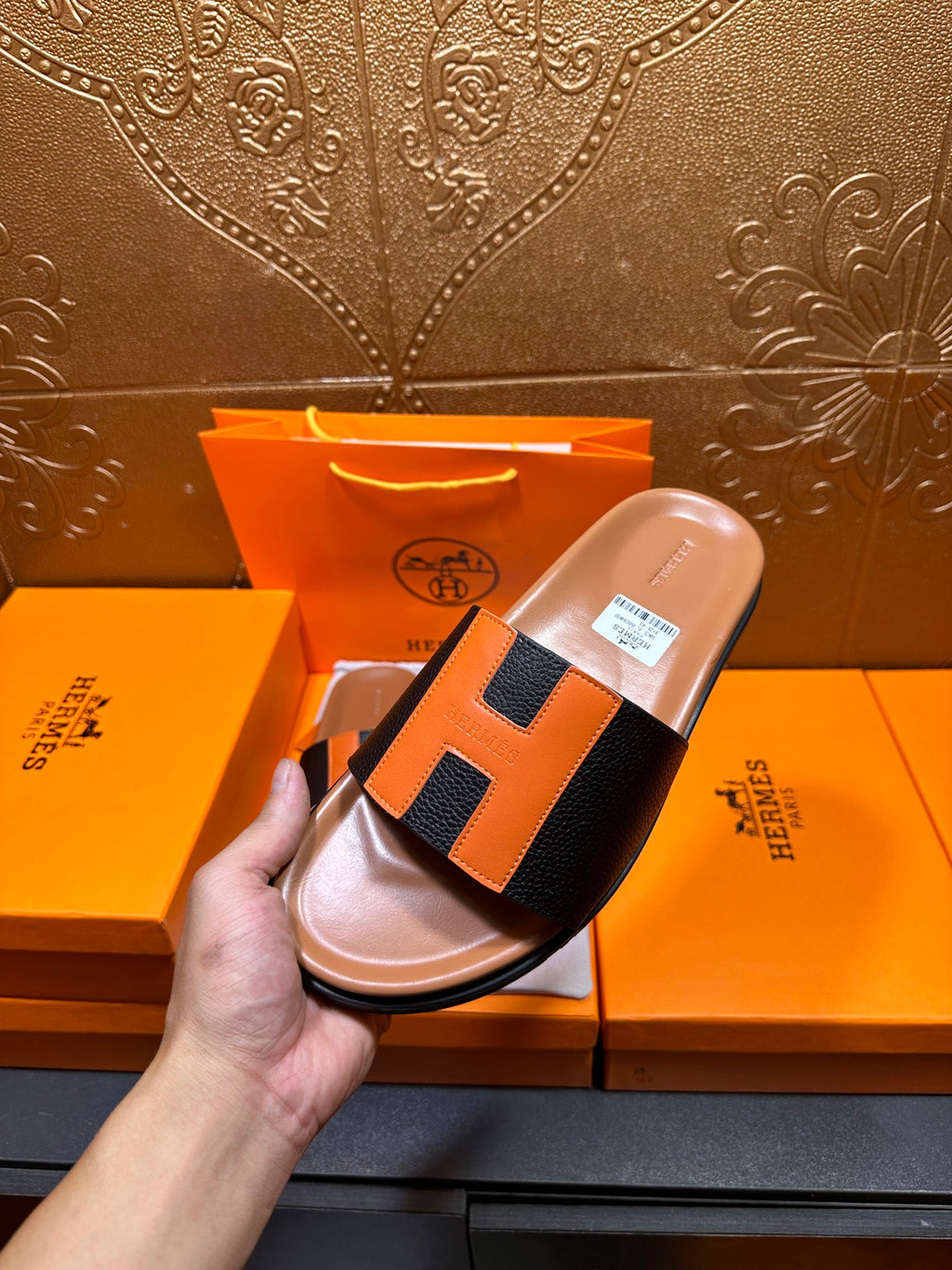 Hermes slide sandals with orange H-style detail on black straps, tan footbeds