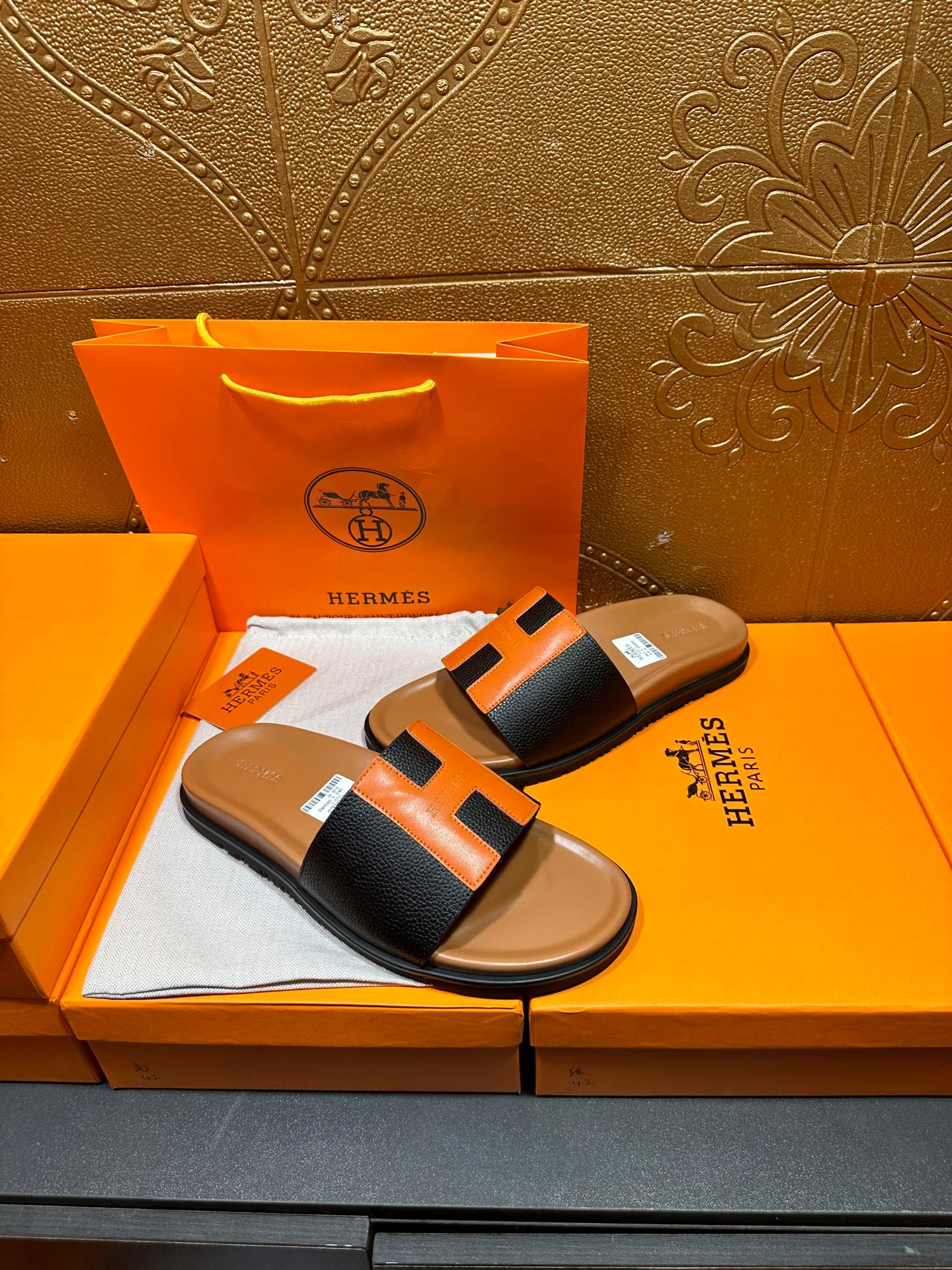 Hermes slide sandals featuring black straps with orange H patch, tan footbed