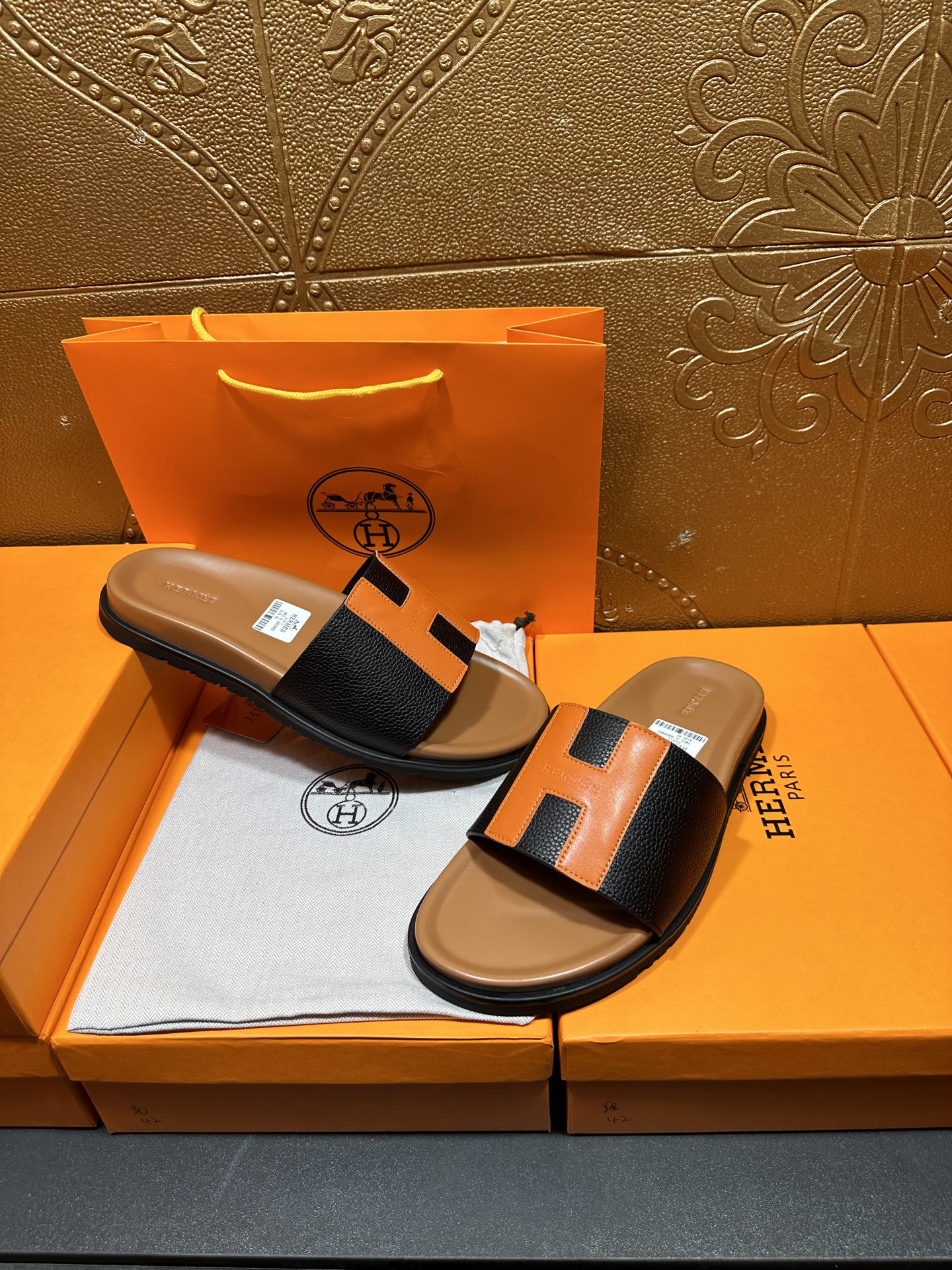 Hermes slide sandals on display: black straps with orange H detail, tan soles