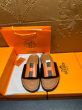 Hermes slide sandals with black straps and orange H-style buckle, tan footbeds