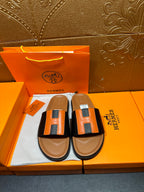 Hermes slide sandals with black straps and orange H-style buckle, tan footbeds