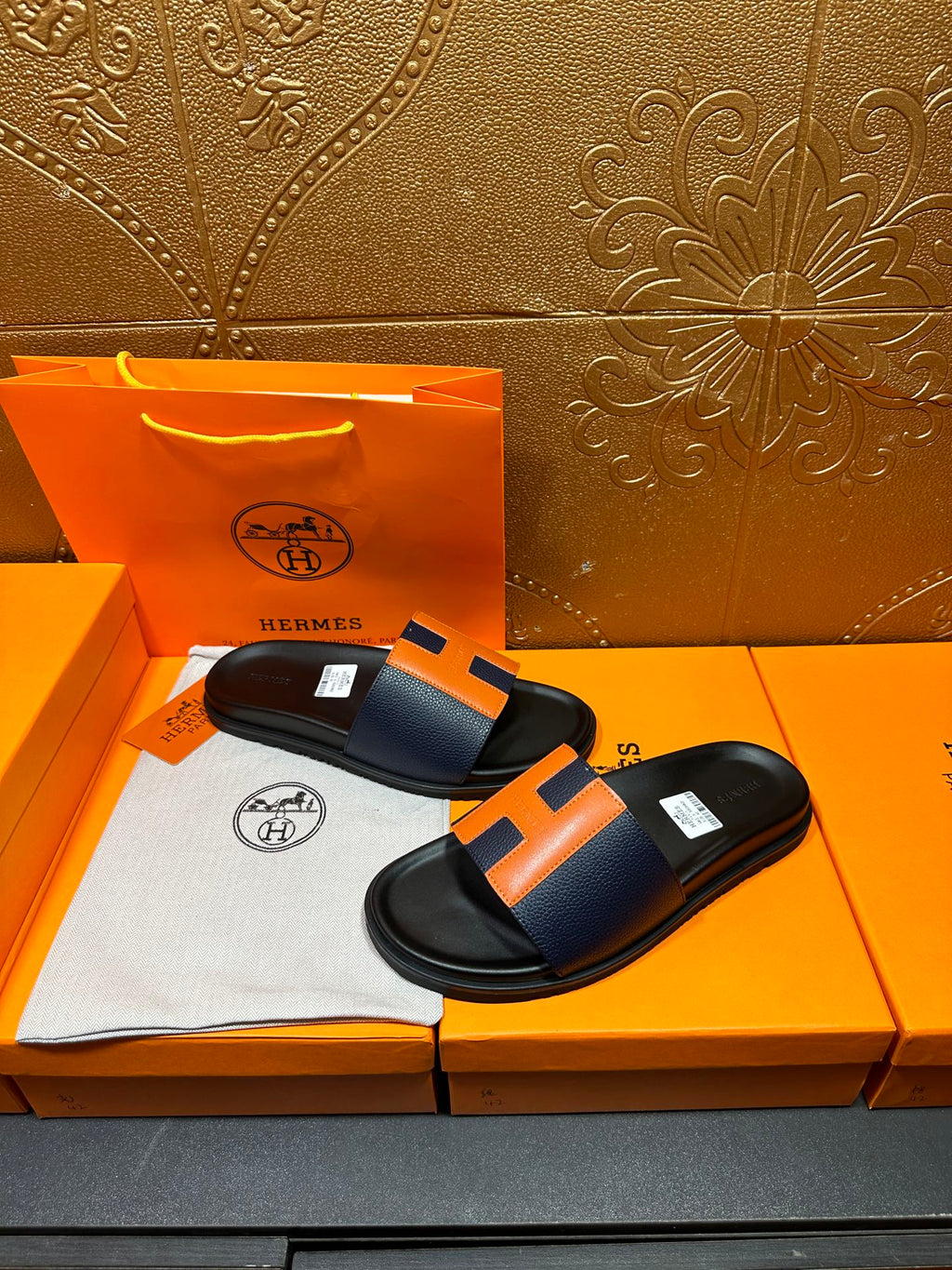 Black slide sandals with orange H strap detail, side view