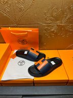 Black slide sandals with orange H strap detail, side view