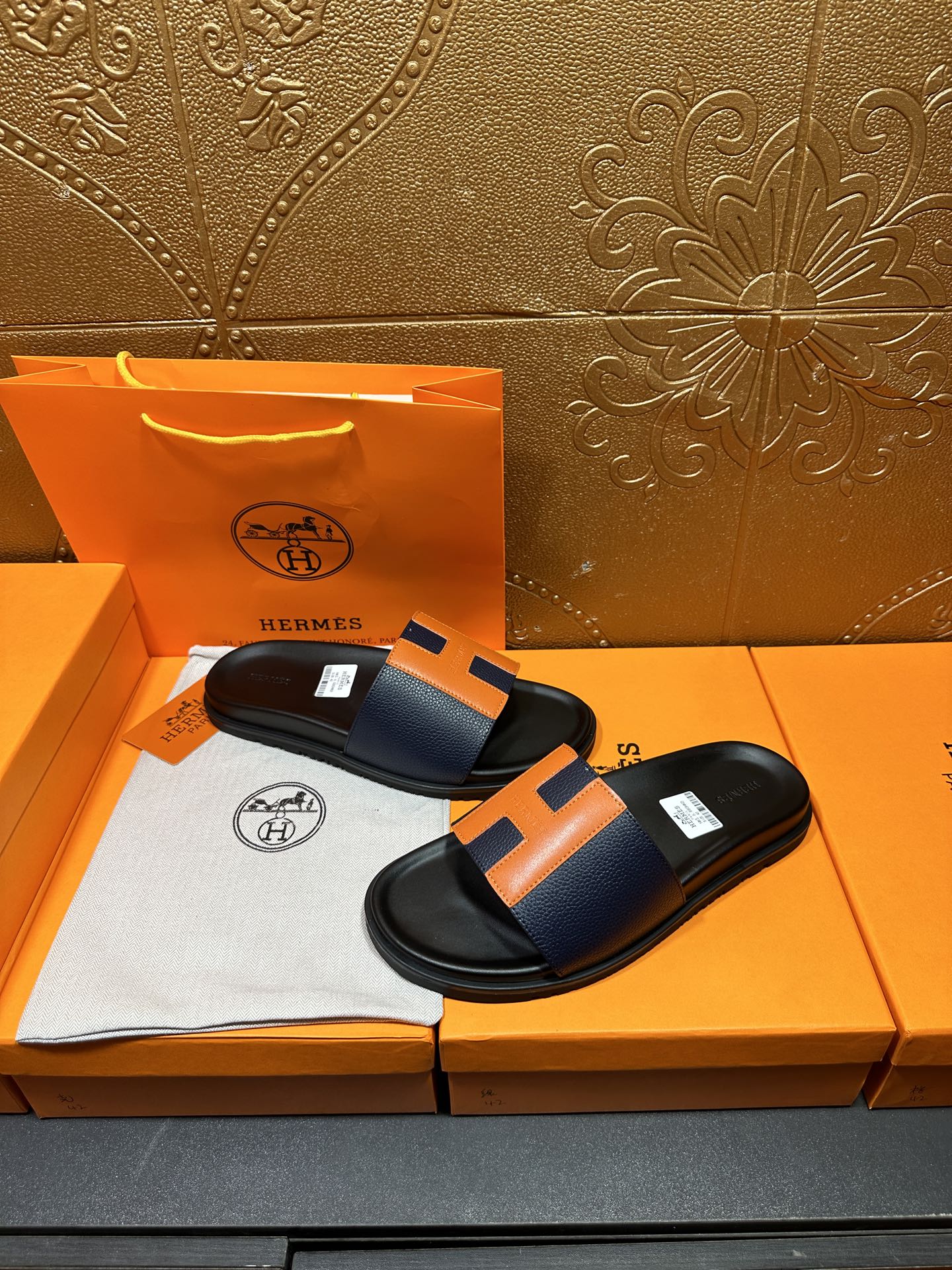 Black slide sandals with orange H strap detail, side view