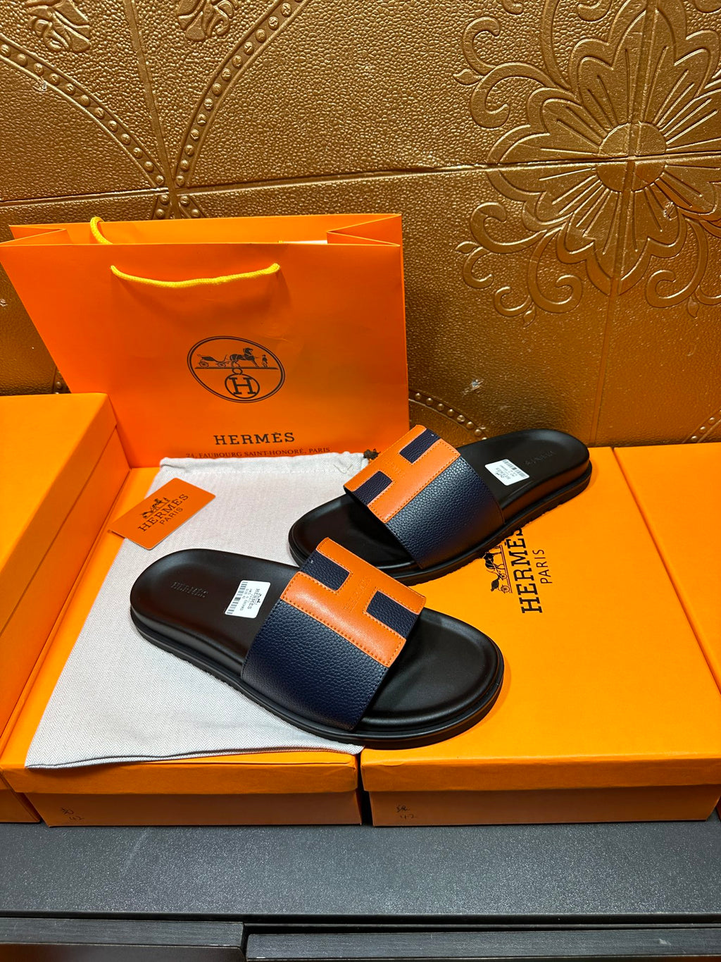 Black slide sandals with orange H strap detail and smooth black footbed