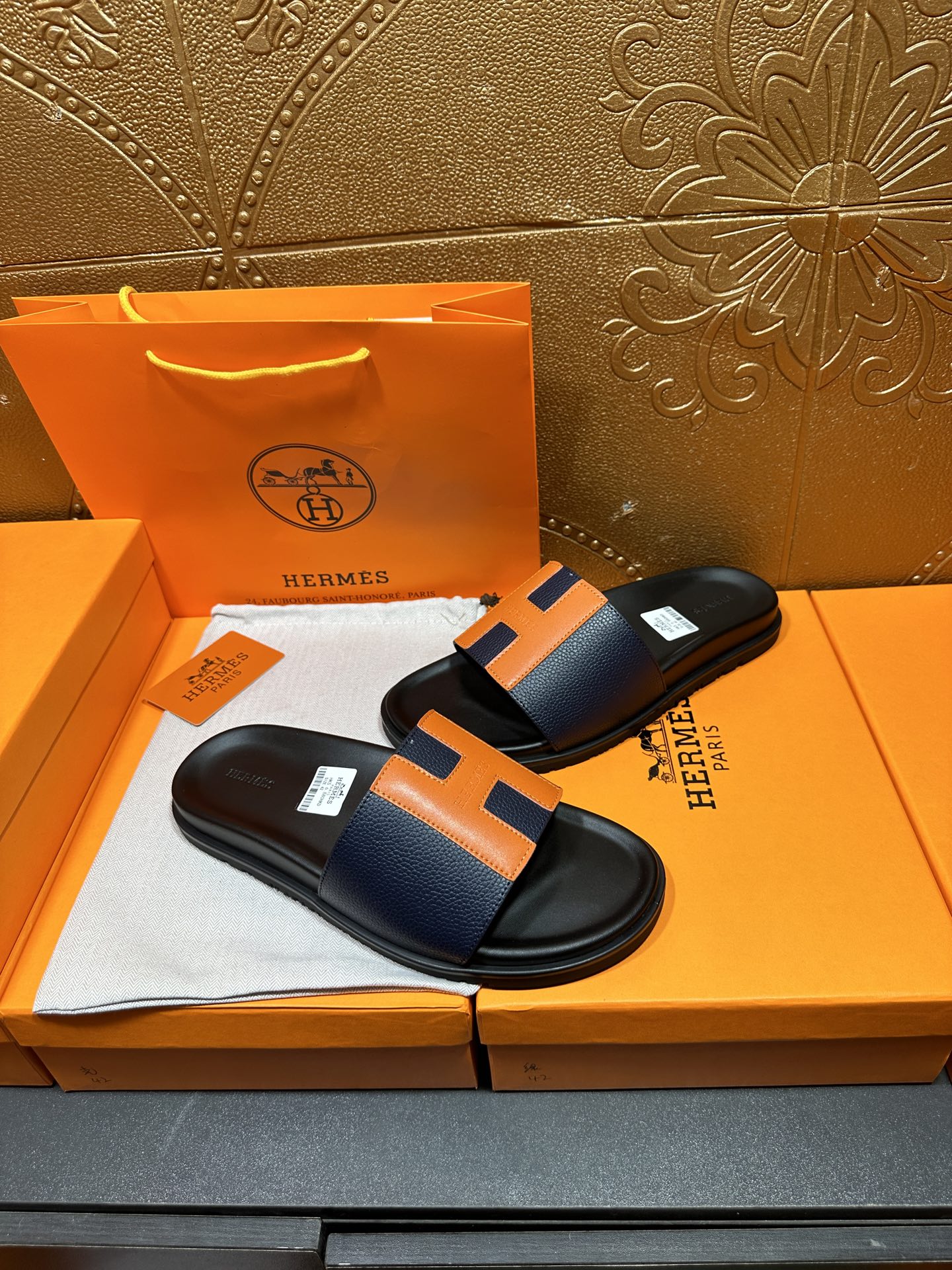 Black slide sandals with orange H strap detail and smooth black footbed