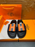 Black slide sandals with orange H strap detail and black footbed