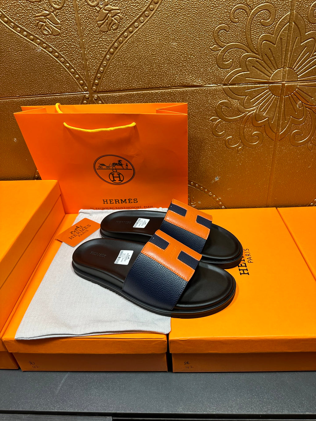 Black slide sandals with orange H strap detail, open toe style