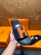 Single sandal held: black slide with orange H strap and black outsole