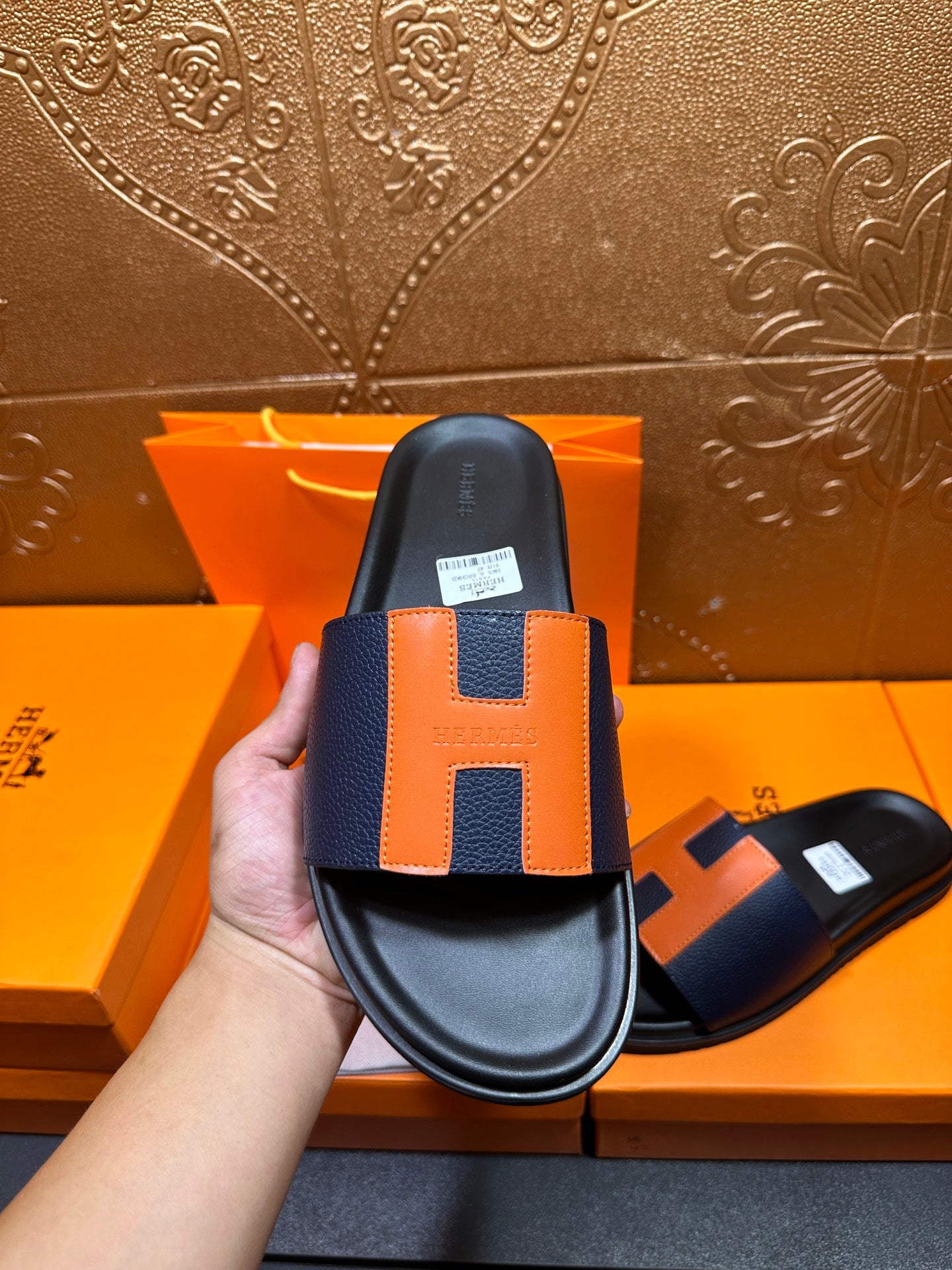 Single black slide sandal with orange H strap detail, top view