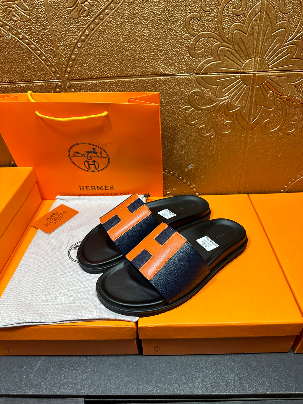Pair of black slide sandals with orange H strap detail on dark soles