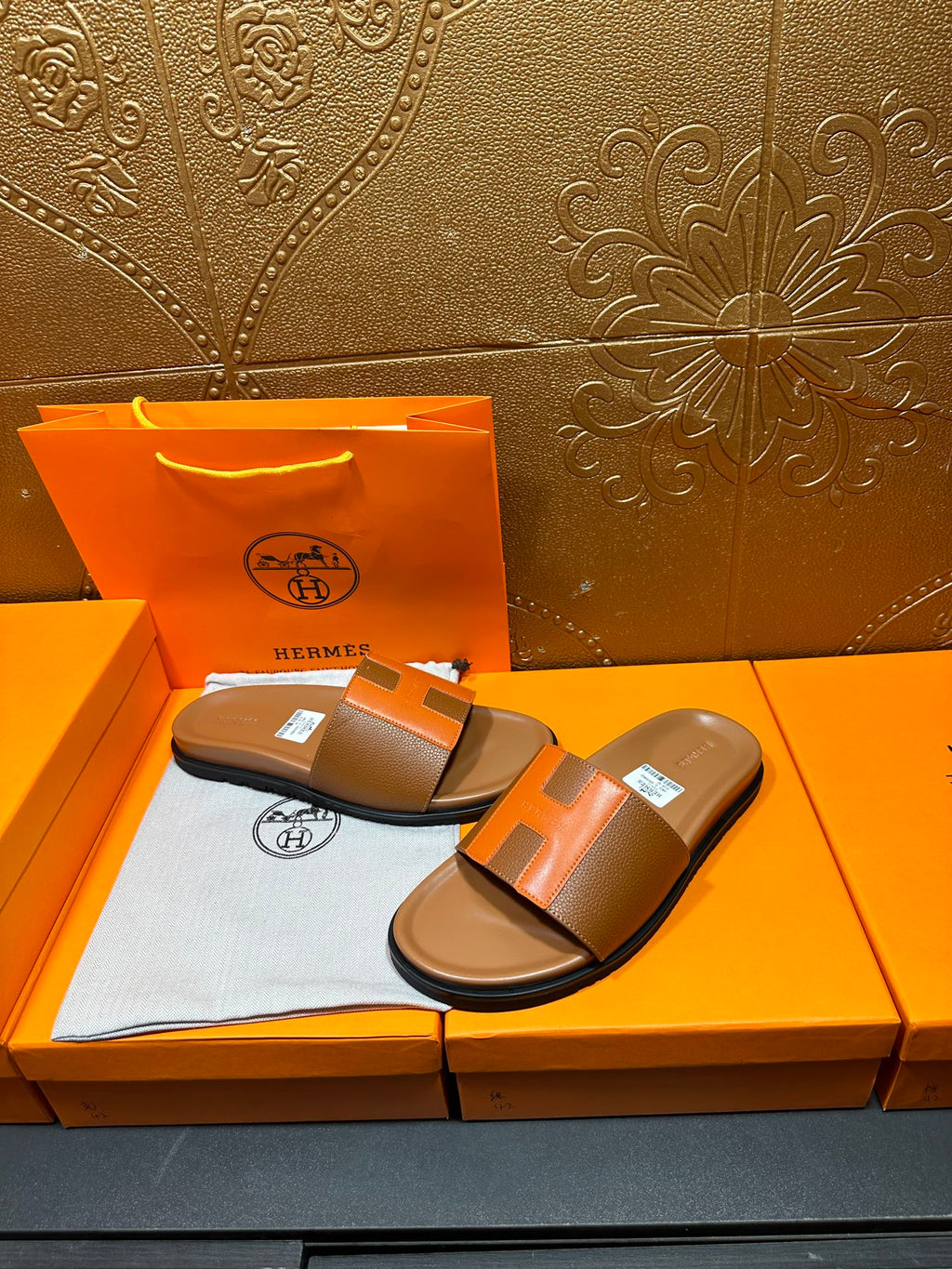 Tan and orange H-strap slide sandals on orange box with tissue lining.