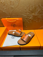 Tan and orange H-strap slide sandals on orange box with tissue lining.