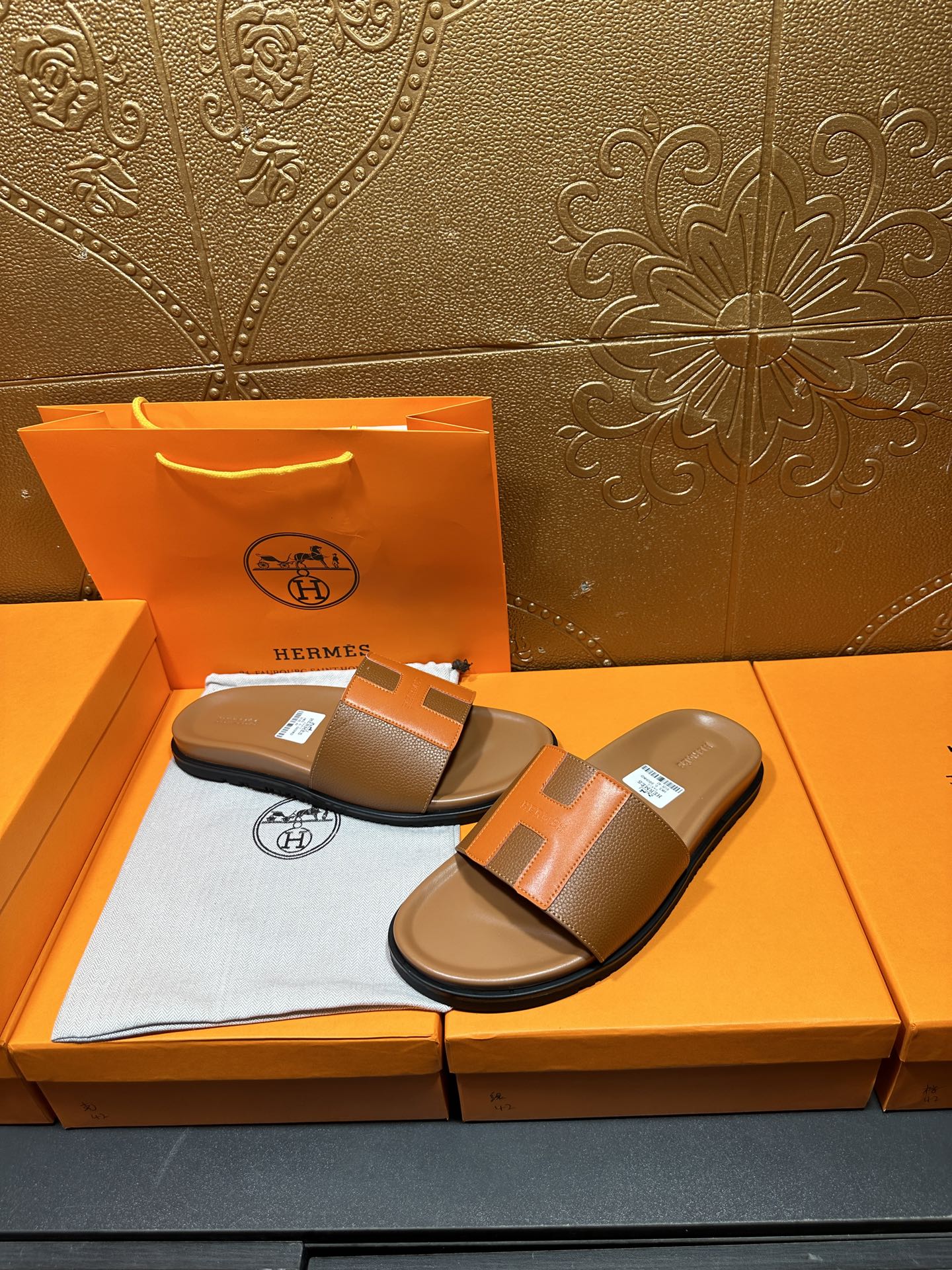 Tan and orange H-strap slide sandals on orange box with tissue lining.