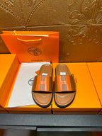 Tan and orange H-strap sandals with black sole, shown in product box.
