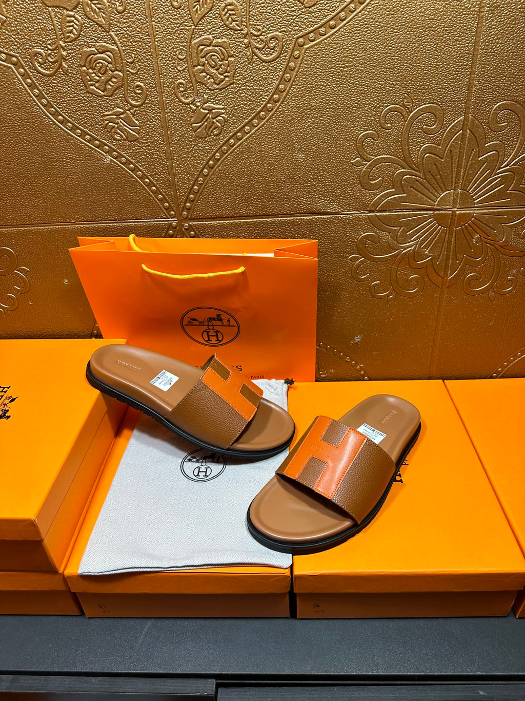 Pair of tan and orange H-strap sandals with black soles on orange box tray.