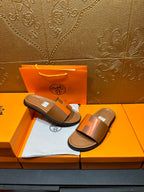Pair of tan and orange H-strap sandals with black soles on orange box tray.