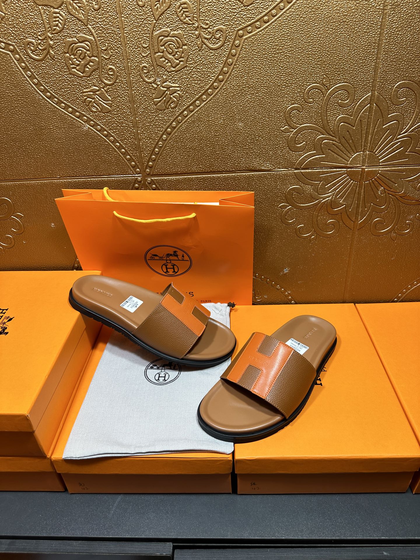 Pair of tan and orange H-strap sandals with black soles on orange box tray.