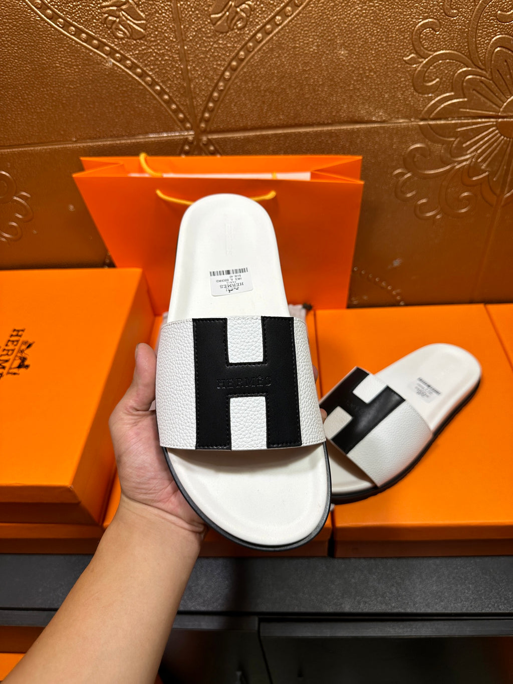 Hermes slide sandal held in hand: white upper with black H cross strap