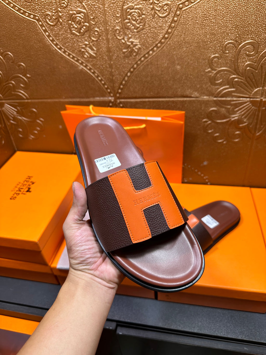 Single leather slide sandal in hand, dark brown base with orange H strap