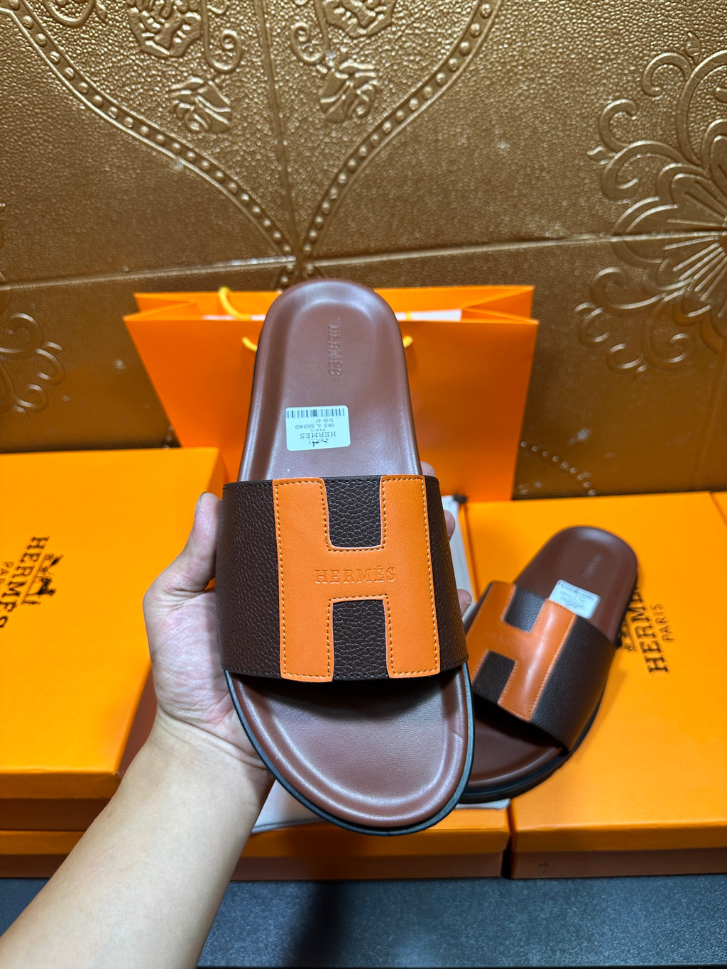 Front view leather slide sandal in hand, dark footbed with orange H strap detail