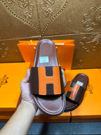 Front view leather slide sandal in hand, dark footbed with orange H strap detail