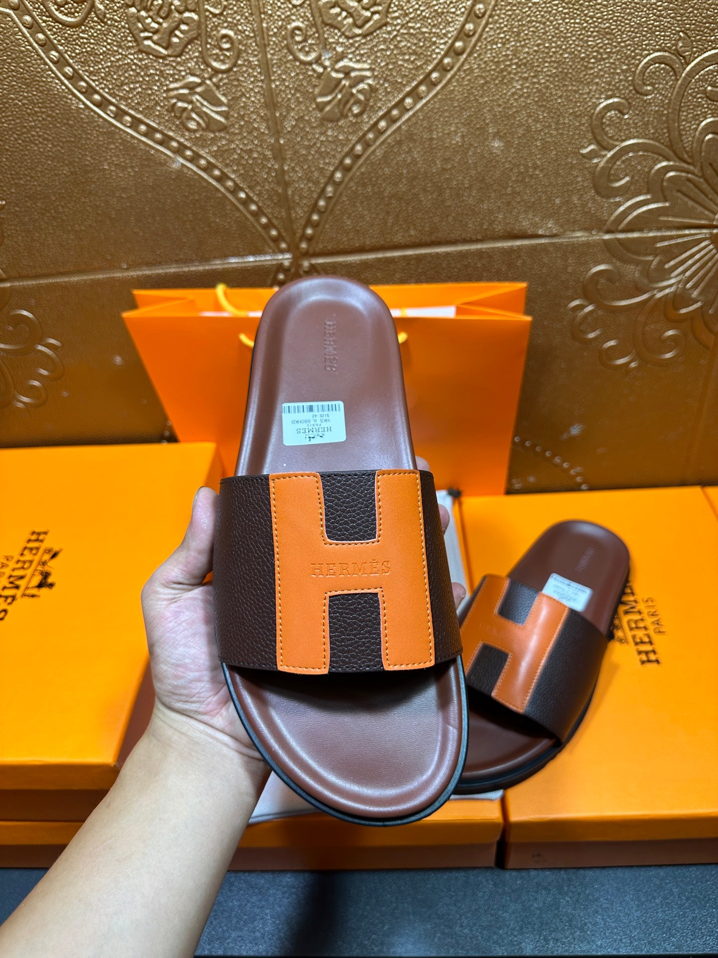 Front view leather slide sandal in hand, dark footbed with orange H strap detail