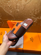 Leather slide sandal held in hand, dark footbed with orange H strap detail