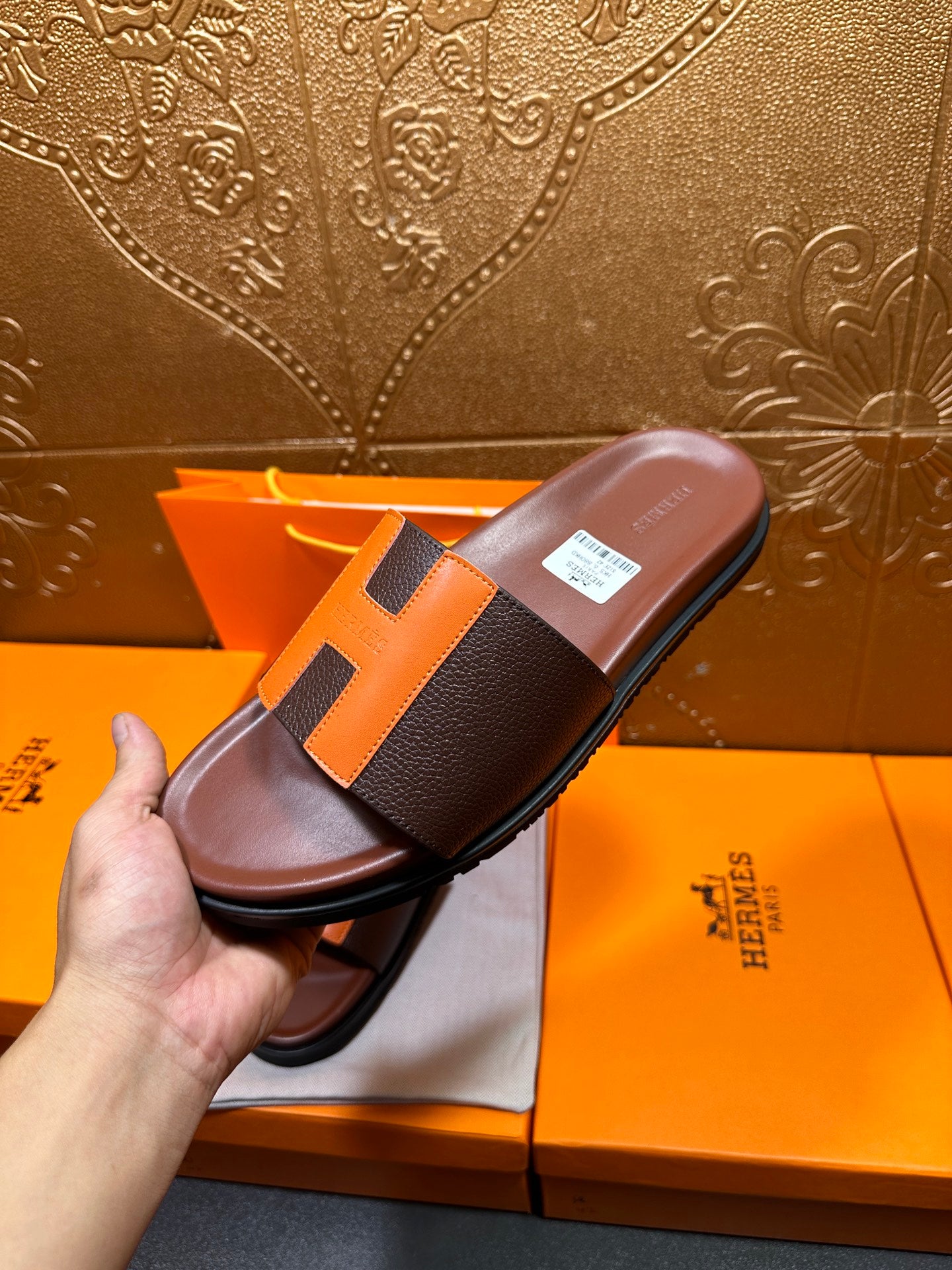Leather slide sandal held in hand, dark footbed with orange H strap detail