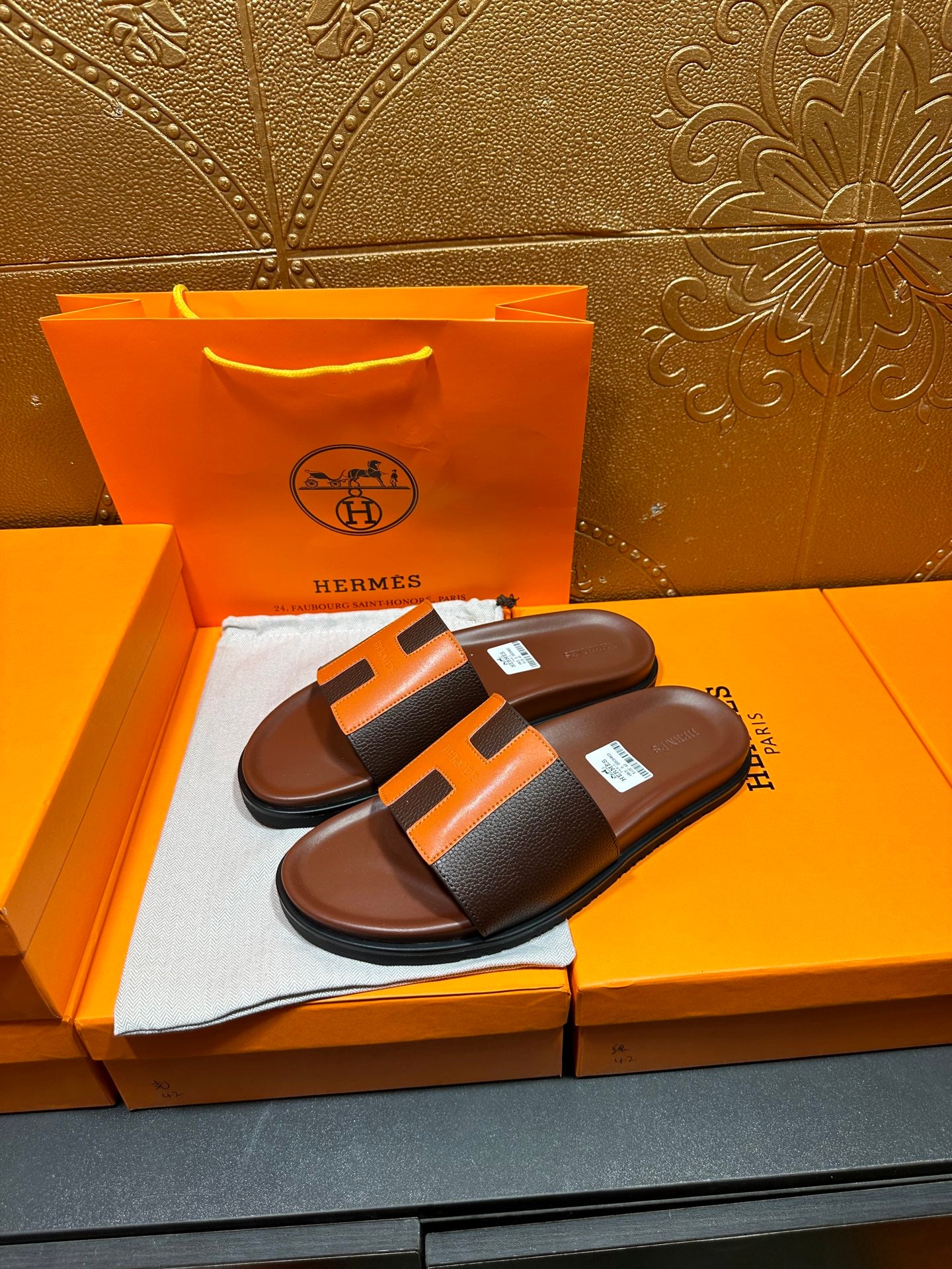 Leather sandals with orange H strap detail and dark footbed, pair on display box