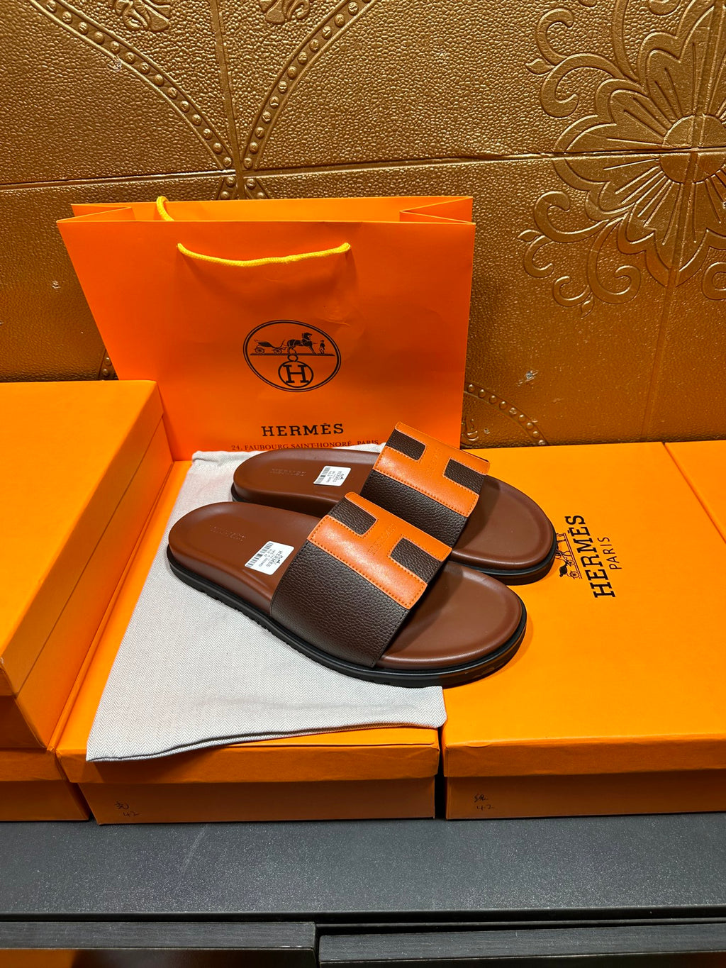 Leather sandals with orange H strap detail and dark footbed, single pair on box