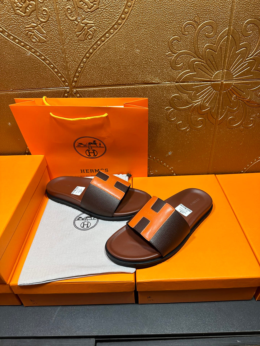 Leather sandals with orange H strap detail, dark footbed, pair resting on box