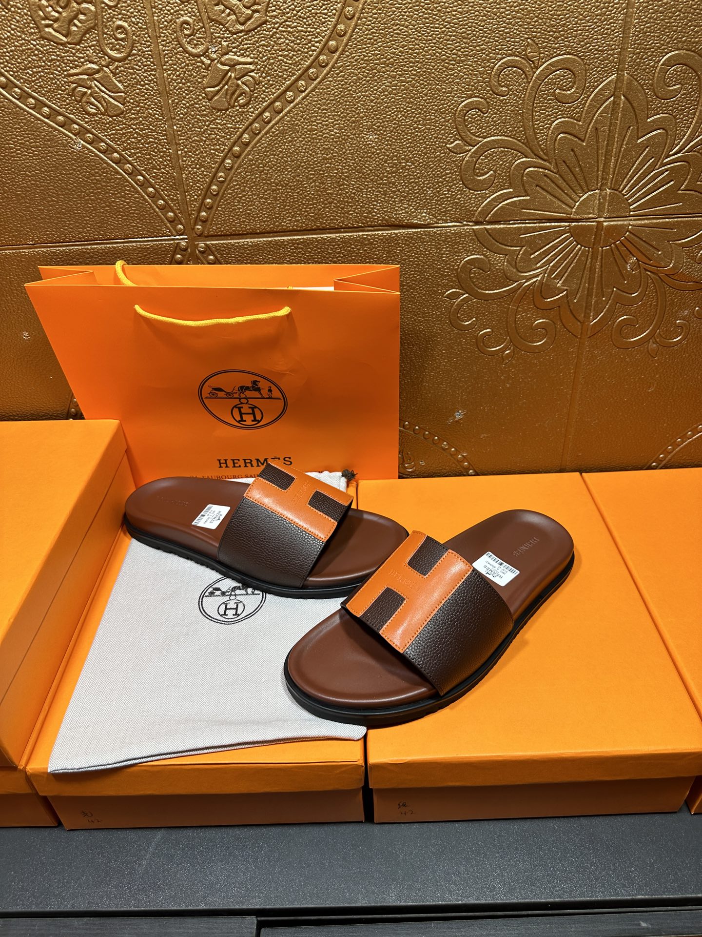 Leather sandals with orange H strap detail, dark footbed, pair resting on box