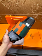 Hermes slide sandal close-up, green strap with orange H blocks over black footbed.